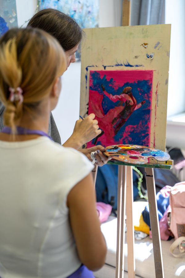 Over the student’s shoulder: the teacher shows on the canvas how to paint the figure.