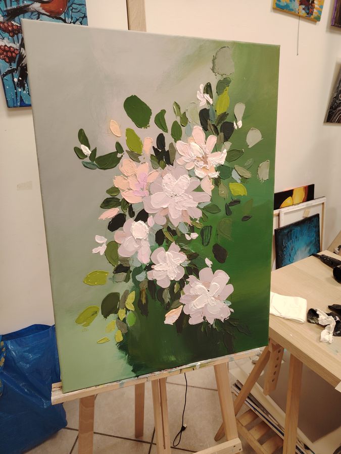 An impasto painting of white blossoms on a green ground on a studio easel.