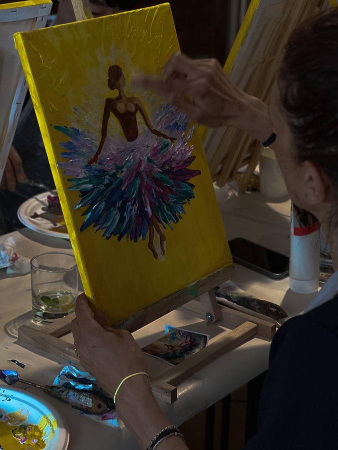 A finished ballerina painting on a yellow canvas, on a table easel at the end of an acrylic evening.