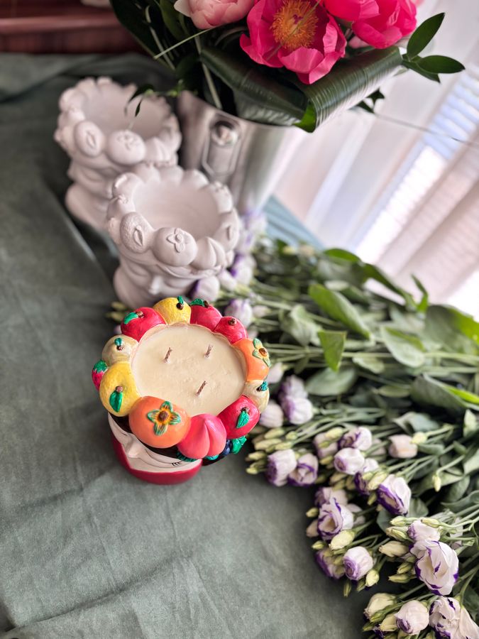 A container candle with a painted fruit rim among lisianthus stems.