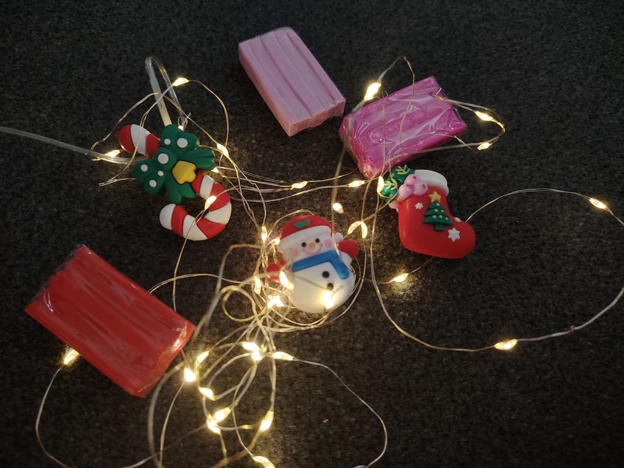 Polymer-clay Christmas ornaments — a candy cane, a snowman, a stocking — among fairy lights.