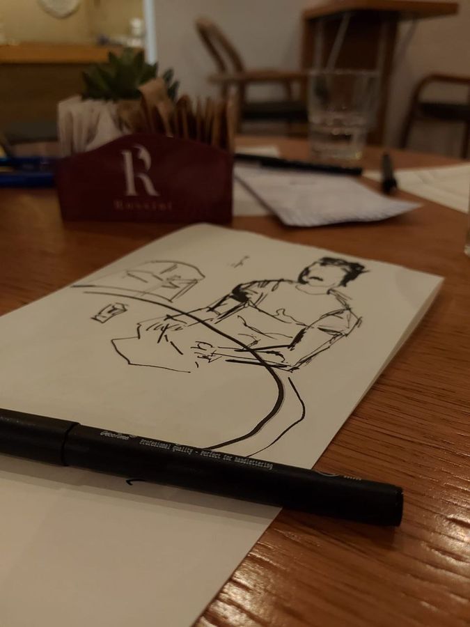 A loose ink sketch of a seated figure on a café table next to a brush pen.